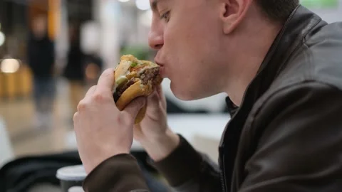 A man eats a juicy burger in a fast food restaurant, close-up Stock-Footage 237389680