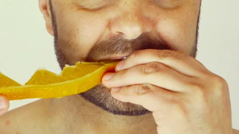 A man eats a juicy slice of orange. Close-up, light background Vídeo Stock 107501290