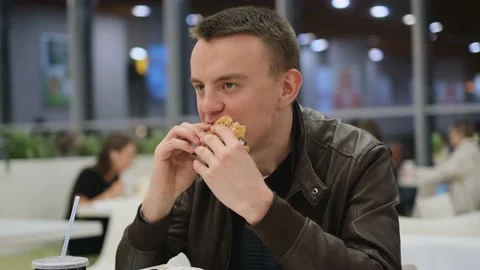A man eats a juicy tasty burger in a fast food restaurant, close-up Stock Footage 237389889