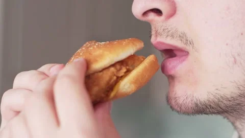 A man eats junk food, a close-up. Guy slowly bites chicken burger Stock Footage 131992104