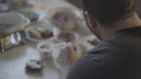 A man eats meat, puts sauce on a piece of meat, watches a movie on a smartphone Stock Footage 129101364