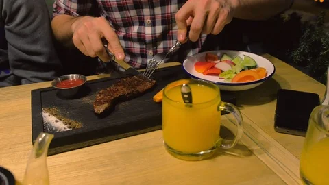 Man eats medium-roasted beef steak served on a black wooden Board in cafe. Stock-Footage 119006552