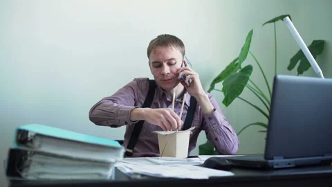Man Eats Noodles in Office and Talking on a Phone Stock Footage 104019988