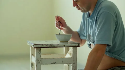 Man eats noodles while sitting at an old and dirty chair , on a light background Stock Footage 132036527