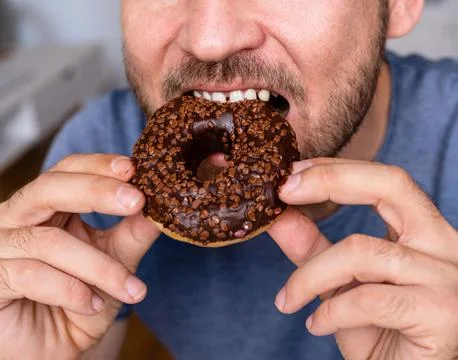 Man eats pink coloured chockolate donut closeup. Stock Photos