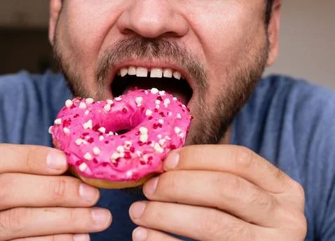 Man eats pink coloured doughnut closeup mouth. Stock Photos