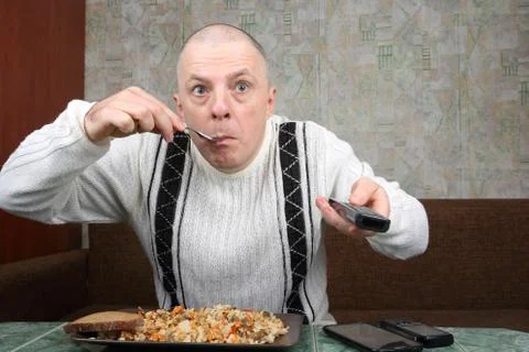 The man eats rice pilaf and stares of TV program Foto stock