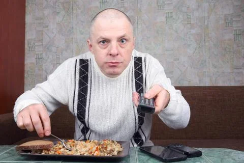 The man eats rice pilaf and stares of TV program Stock Photos