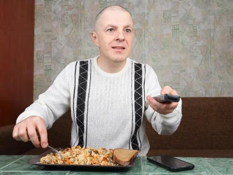 The man eats rice pilaf and stares of TV program Foto stock