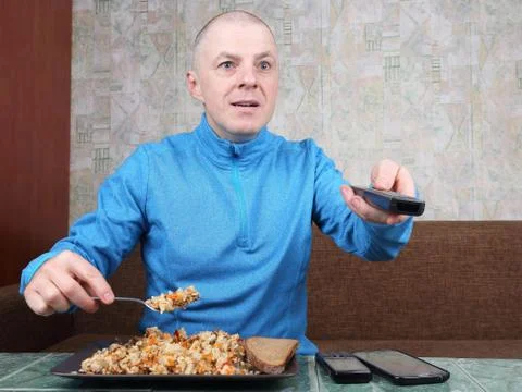 The man eats rice pilaf and stares of TV program Foto stock
