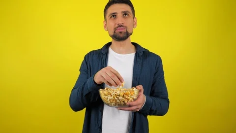 Man eats savoring popcorn from a transparent glass plate, smiles and like it Stock Footage 119865374