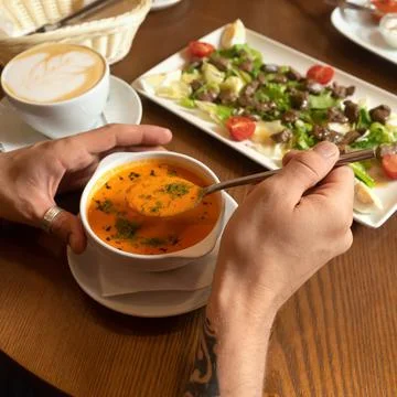 Man eats set menu sitting at wooden table. Male hands hold spoon and white Stock Photos