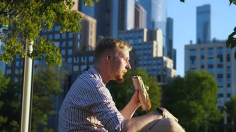 A man eats shawarma and drinks water in the background of skyscrapers Stock Footage 202393119