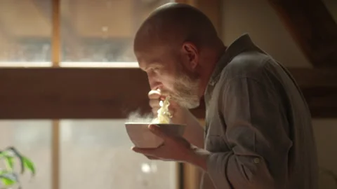 Man eats a steaming bowl of noodles while having a video chat meeting Video stock 133293692