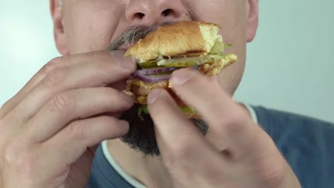 A man eats a vegetarian burger greedily. Hungry middle-aged man eating a burger Stock Footage 145109262