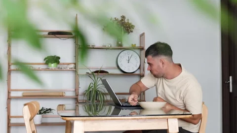 Man eats while working on his laptop in living room. Stock Footage 310948240