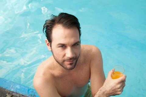 Man in the edge of the pool drinking juice Stock Photos