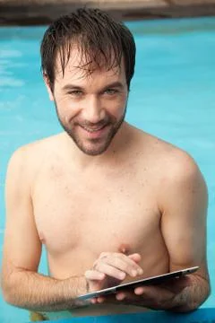 Man in the edge of the pool using a tablet Foto stock