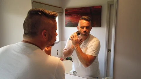 Man with an electric razor in the mirror shaving Just touching up a few Stock Footage 121871388