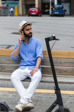 Man with electric scooter on a bench while talking on his cell phone Stock Photos
