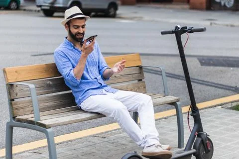 Man with electric scooter on a bench while talking on his smartphone Stock Photos