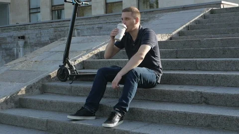 A man with electric scooter sitting with coffee Video stock 115366830