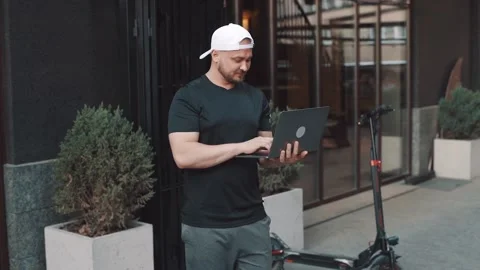 Man with electric scooter working with his laptop in the street in the city 動画素材 229257599