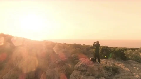 Man in elegant suit with briefcase looking through binoculars on top of a cliff Stock Footage