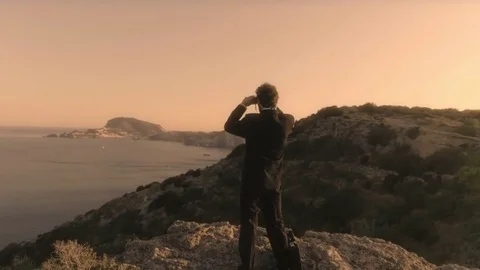 Man in elegant suit with briefcase looking through binoculars on top of a cliff 스톡 동영상 78038976