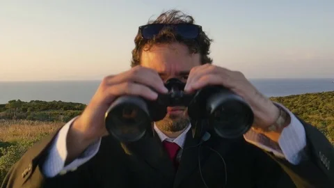 Man in elegant suit with briefcase looking through binoculars on top of a cliff Vídeo Stock 80231211