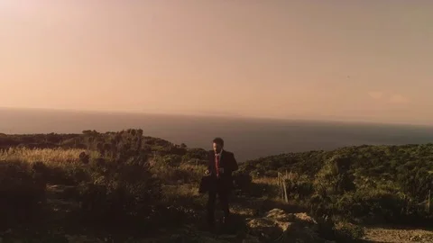 Man in elegant suit with briefcase running on top of a cliff on an island and Stock Footage 78024816