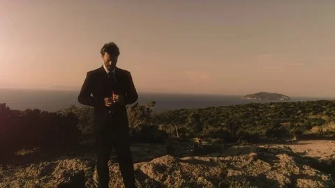 Man in elegant suit straightens his jacket on top of a cliff on an island Stock Footage
