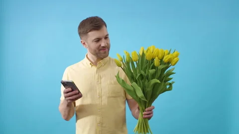 Man embracing technology against a blue canvas with yellow flowers Video stock 273789857