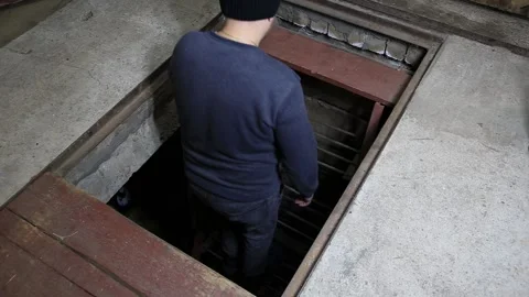 Man emerges from dark underground cellar via steep metal ladder, ascending to Stock Footage 329622212