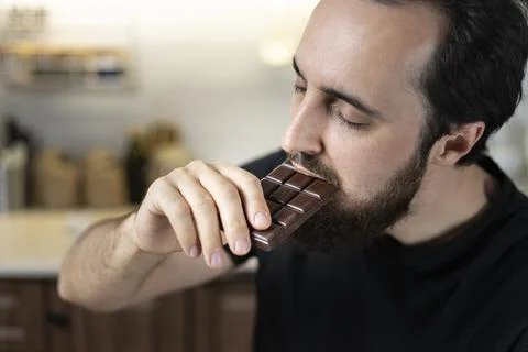 A man emotionally eats chocolate bars at home in the kitchen. Stock Photos