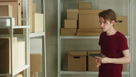 Man employee of warehouse checking parcels on storage and writing information Stock Footage 157504496