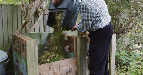 A man emptying freshly cut grass from a grass box into a composting heap Stock Footage 163348883