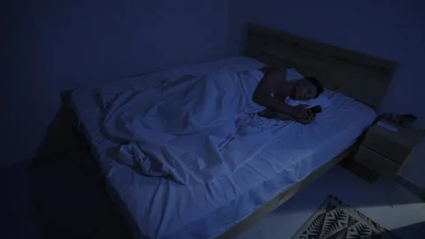 Man endlessly scrolling short form videos on smartphone in bed at night Vídeos de archivo 346248332