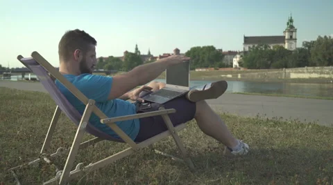 Man ends typing on laptop and chilling out on sunbed by the river. Vídeo Stock 65205357