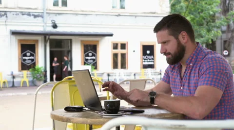 Man ends work on laptop, drinks coffee and smiles for camera in cafe, Vidéo 67631765