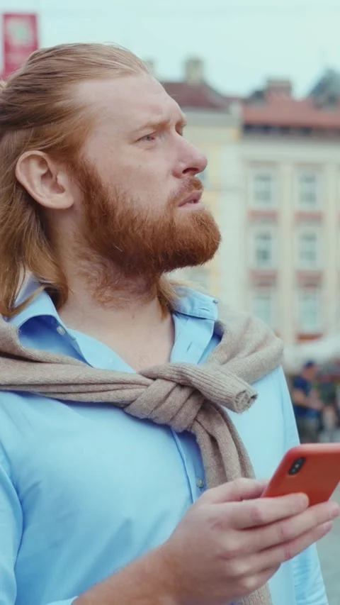 A man is engaged with his smartphone in a bustling city setting, enjoying the Vídeo Stock 314356830
