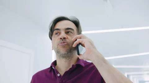 A man is engaged in a phone conversation, surrounded by a modern environment Stock Footage 292643875
