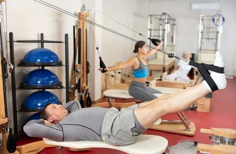 Man is engaged in Pilates simulator with cable and ropes for stretching leg Stock Photos