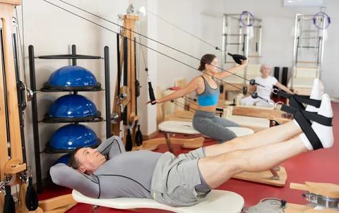 Man is engaged in Pilates simulator with cable and ropes for stretching leg Stock Photos
