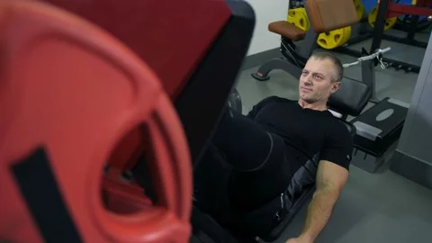 A man is engaged on the simulator. Raises weight with legs 4K Slow Mo Видео 100260431