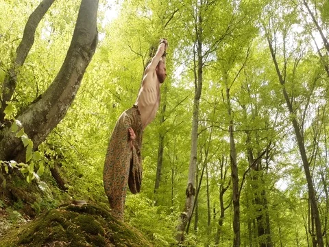 A man is engaged in yoga, standing on one foot under the sun on a mossy rock in Stock Footage
