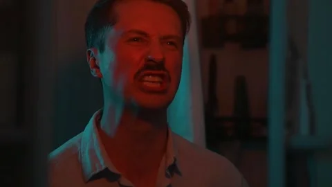 A man engages in a heated discussion in a dark room with colored lighting. His Vidéo 337111829