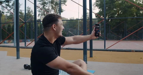 A man is engaging in a video call while he is at a vibrant sports facility Stock Footage 318074928