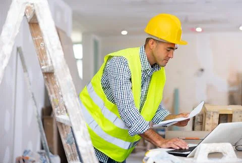 Man engineer checking documents and using laptop during repair works 写真素材