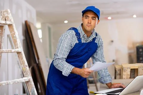 Man engineer checking documents and using laptop during repair works Stock Photos